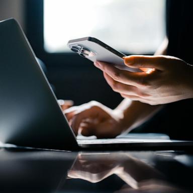PHOTO: Stock photo of a person using their phone and laptop.