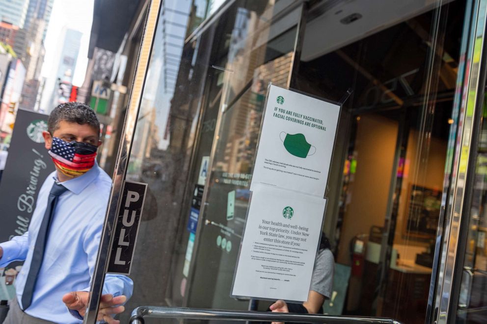 PHOTO: A man with a mask walks out of a Starbucks where a "if you are fully vaccinated, facial coverings are optional" sign is displayed on the door in New York, May 26, 2021.
