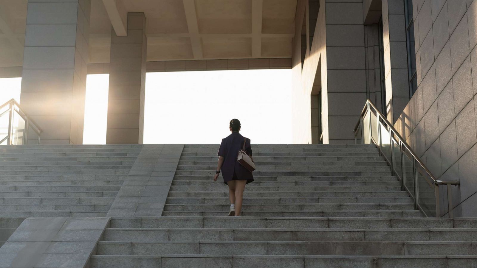 PHOTO: A woman walks up stairs in sunlight.