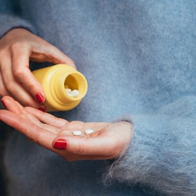 stock photo of a person holding tablets and a medicine bottle, representing personal healthcare, treatment, and responsible medication use at home
