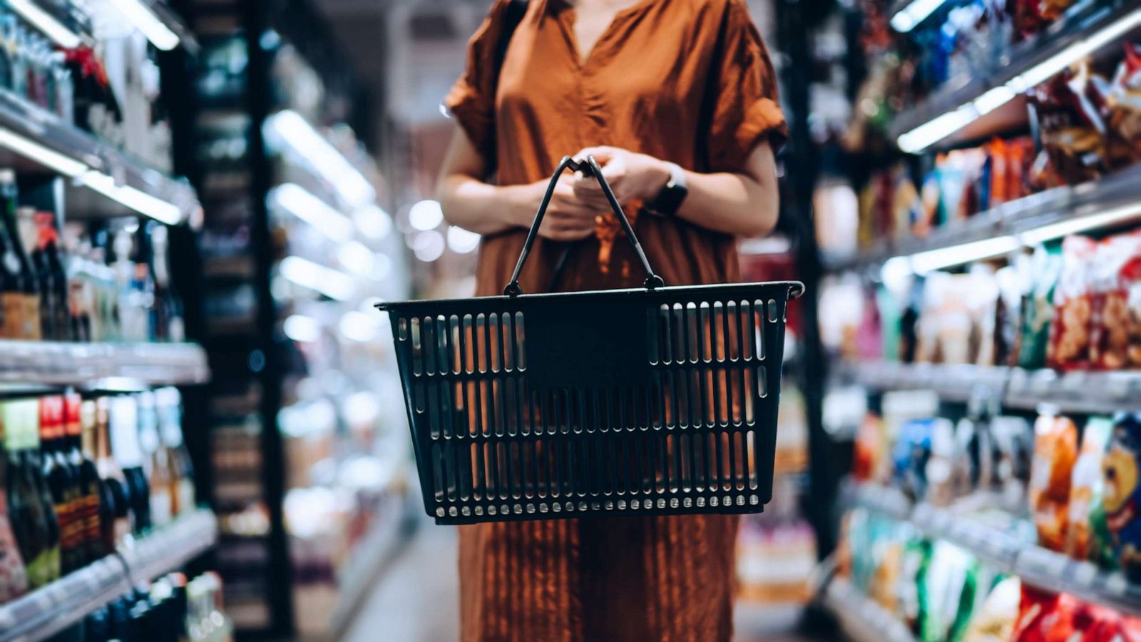 PHOTO: A woman carrying a shopping basket stands along a product aisle in a grocery store.