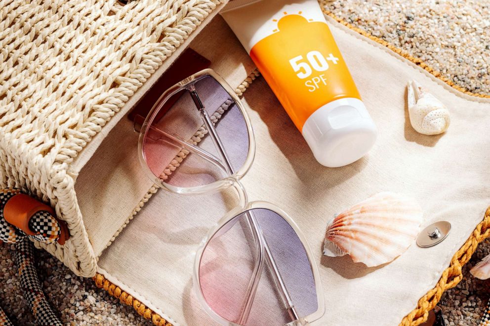 STOCK PHOTO: Sunscreen and glasses in a wicker straw bag on a sandy beach