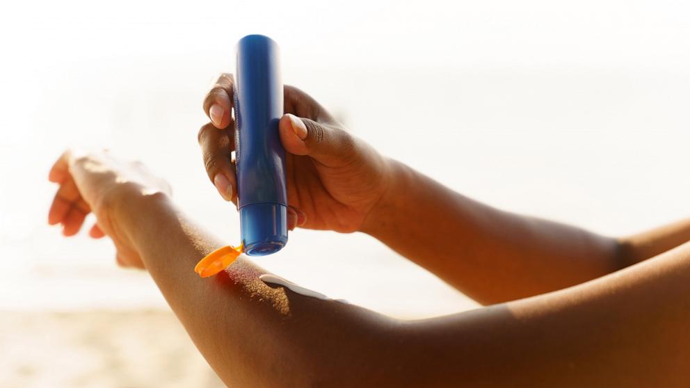 PHOTO: Black woman applying sunscreen lotion on beach.