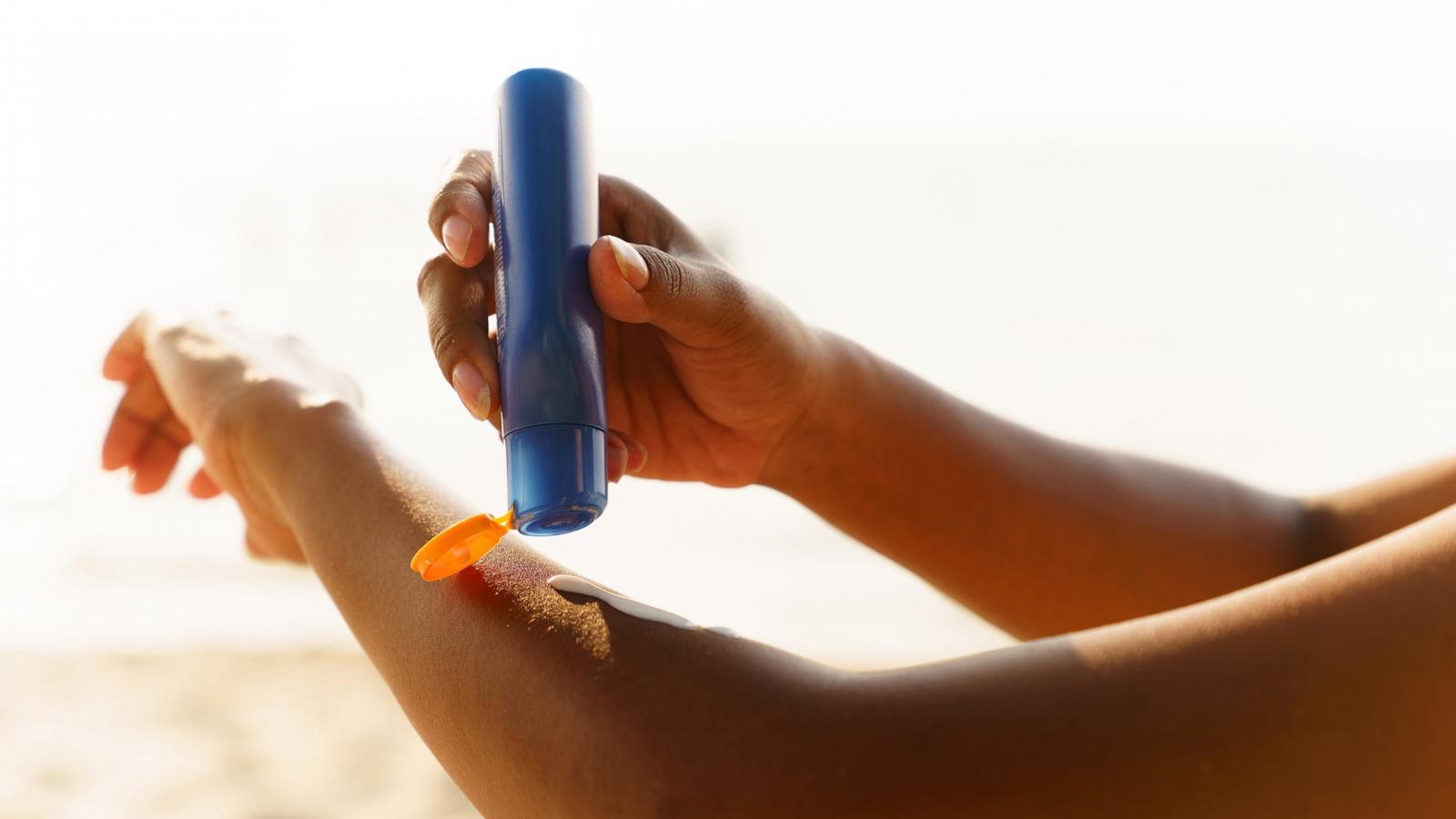 PHOTO: Black woman applying sunscreen lotion on beach.