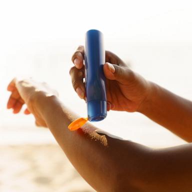 PHOTO: Black woman applying sunscreen lotion on beach.