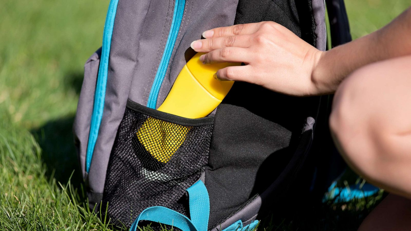 PHOTO: Women's hands put sunscreen in a backpack on the green grass background.