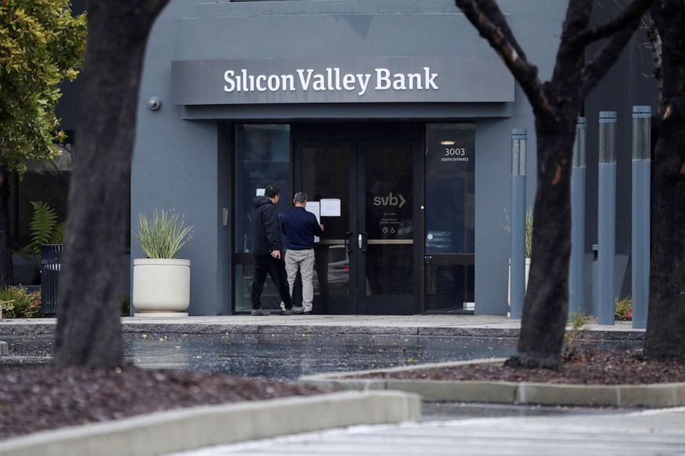 PHOTO: A man puts a sign on the door of the Silicon Valley Bank as an onlooker watches at the bank's headquarters in Santa Clara, Calif., March 10, 2023.