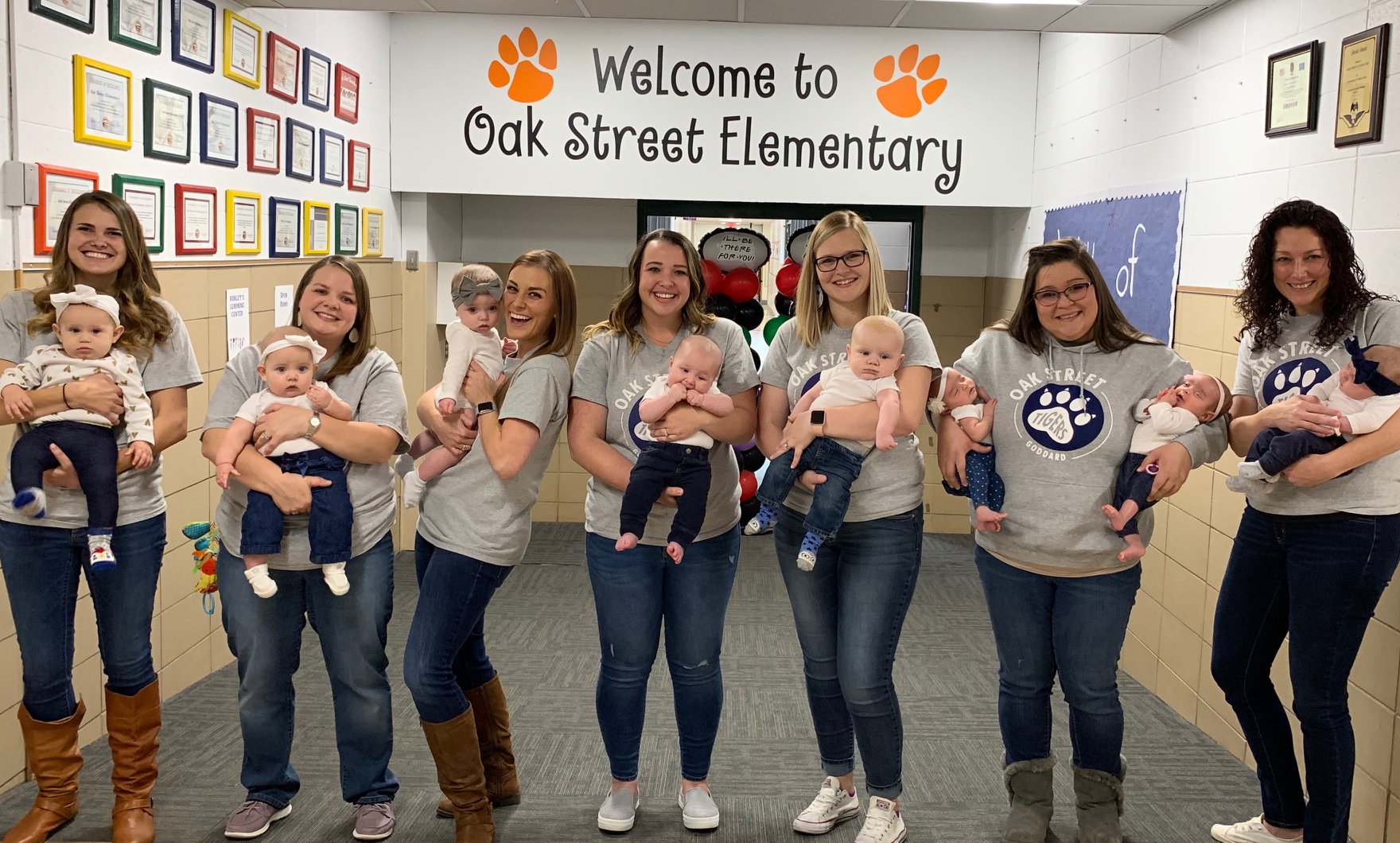 PHOTO: Seven teachers pose with their eight babies in the front hall at Oak Street Elementary in Goddard, Kan.