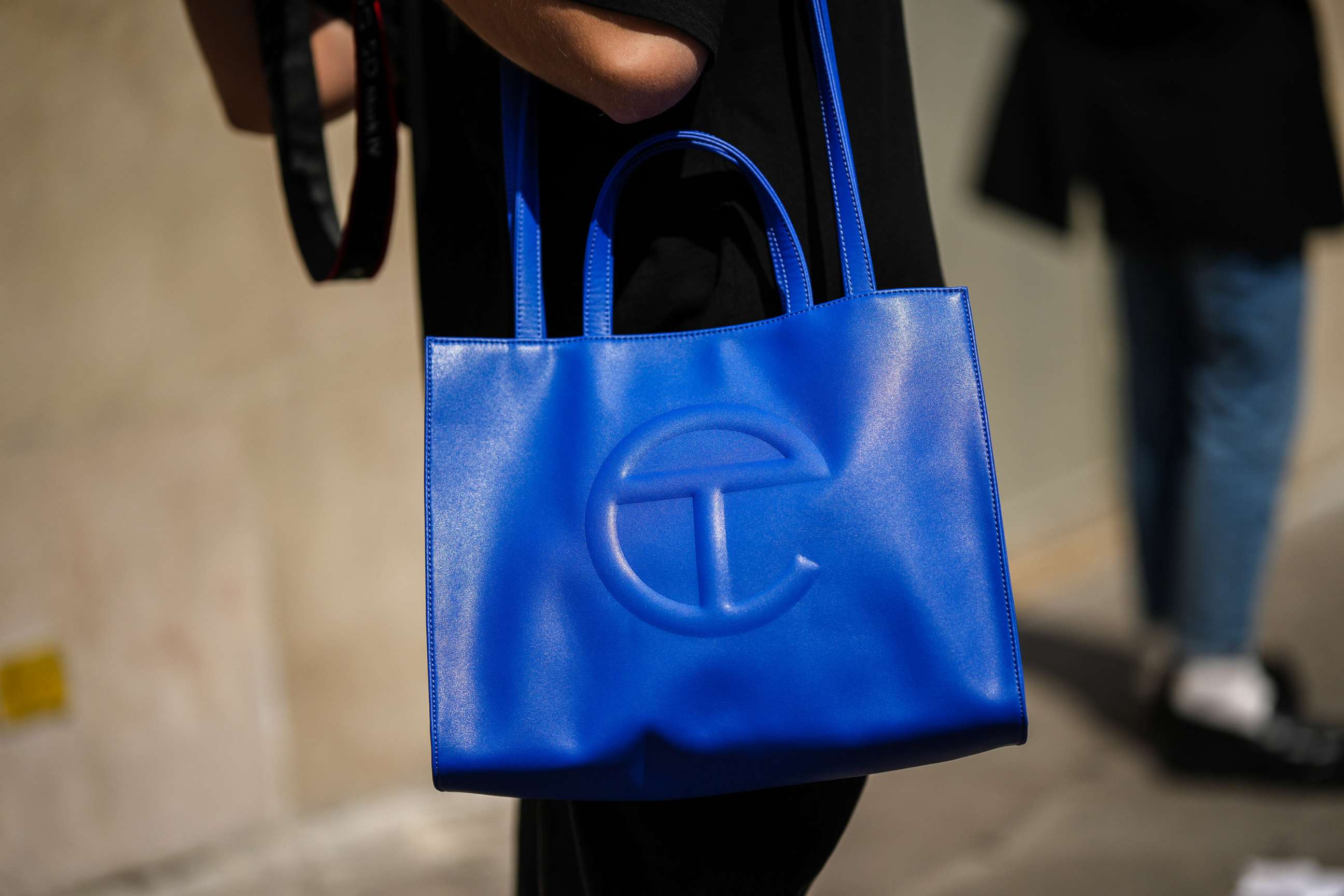PHOTO: A guest wears a royal blue shiny leather Telfar large shoulder bag, during the Bluemarble show, during Paris Fashion Week Menswear Spring Summer 2023, June 21, 2022, in Paris.