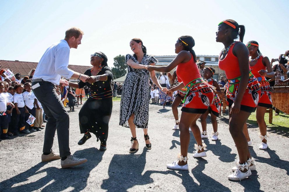 PHOTO: Prince Harry, Duke of Sussex, and Meghan, Duchess of Sussex, dance as they arrive for a visit to "Justice  desk", an NGO in the township of Nyanga in Cape Town, as they begin their tour of the region, Sept. 23, 2019.