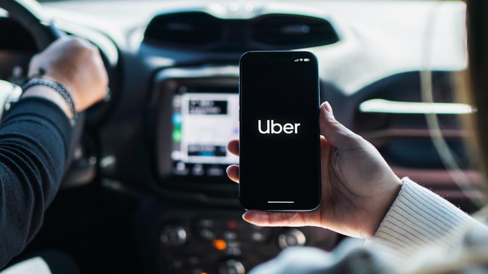 PHOTO: A woman inside car holds a smartphone with Uber app on the screen. 