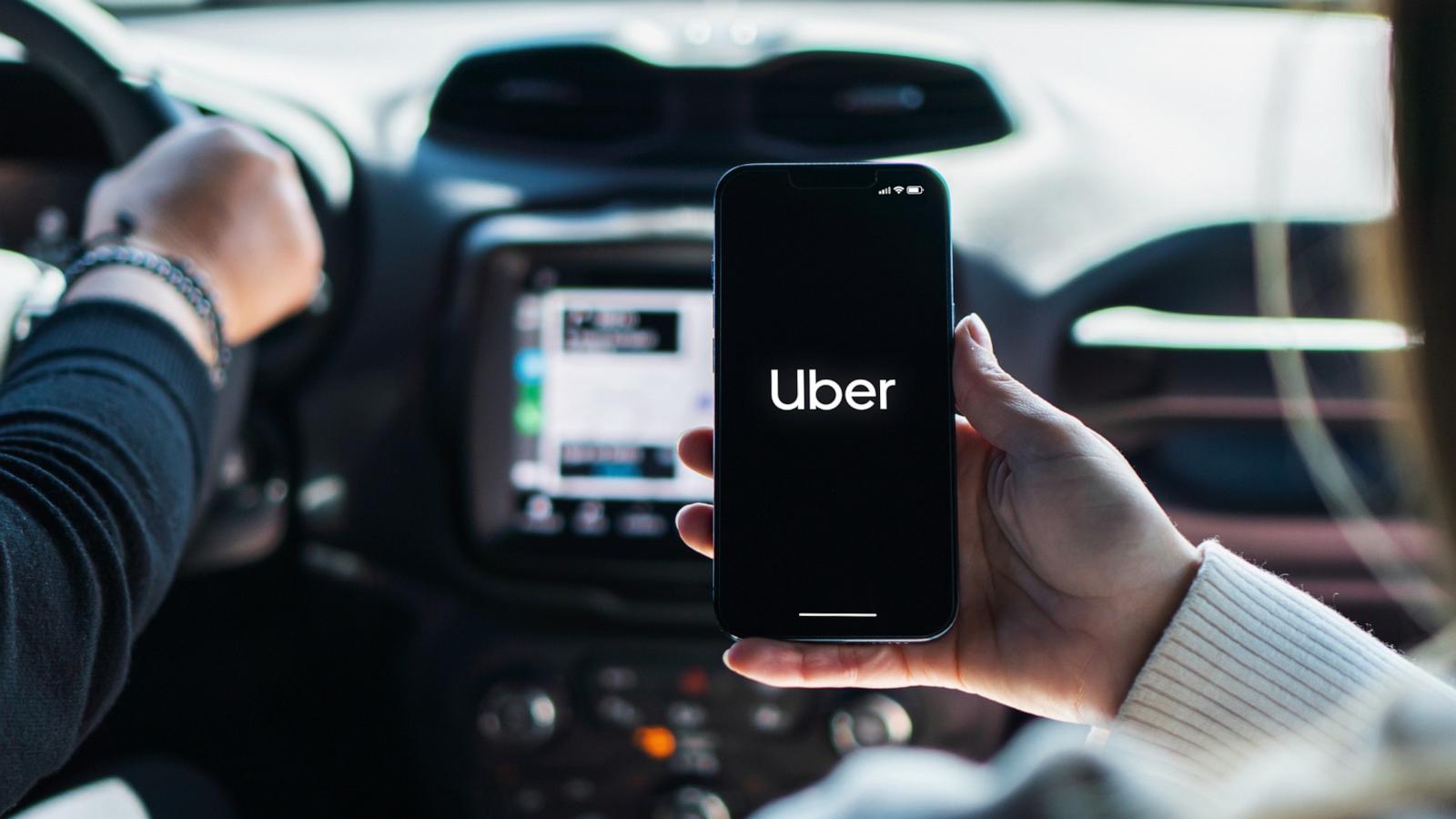 PHOTO: A woman inside car holds a smartphone with Uber app on the screen.