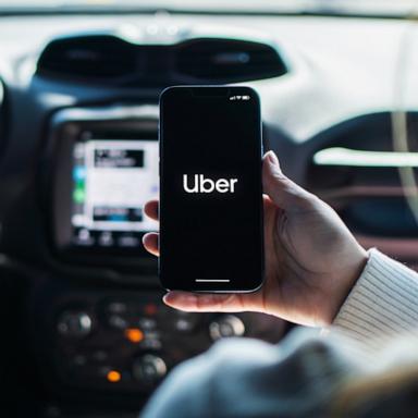 PHOTO: A woman inside car holds a smartphone with Uber app on the screen. 