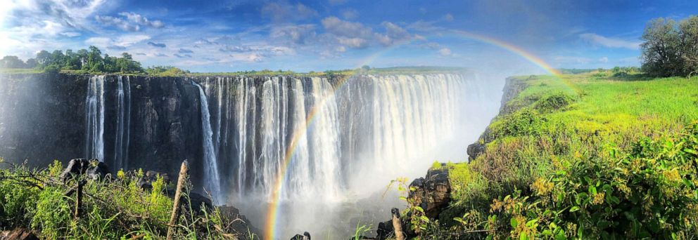 PHOTO: Rainbow extends above Victoria Falls on a sunny day. 