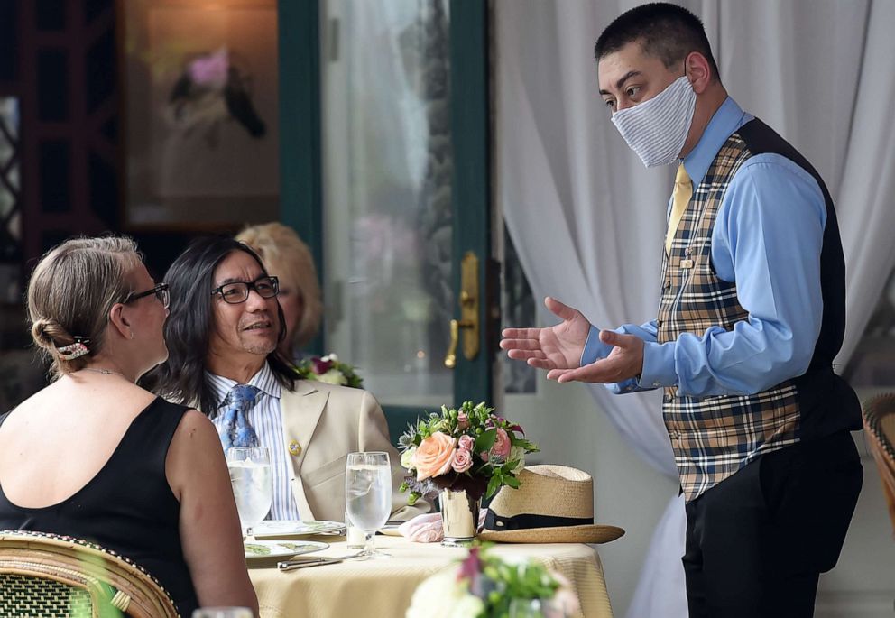 PHOTO: A waiter from The Inn at Little Washington, one of the countrys most renowned restaurants, wears a face mask while talking to customers on the first day of Virginia's phase one reopening in Washington, Va., on May 29, 2020.