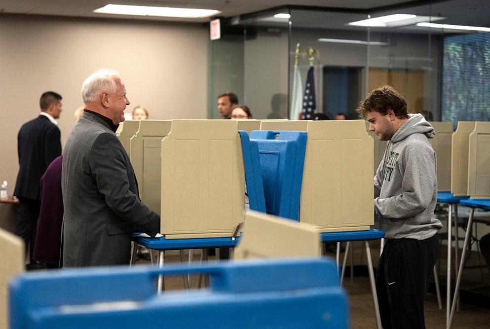 PHOTO: Minnesota Governor and Vice Presidential candidate Tim Walz, left, chats with his son, Gus Walz, a first time voter, as they cast their ballots during early voting at Ramsey County Elections in St. Paul, Minn., on Oct. 23, 2024. 