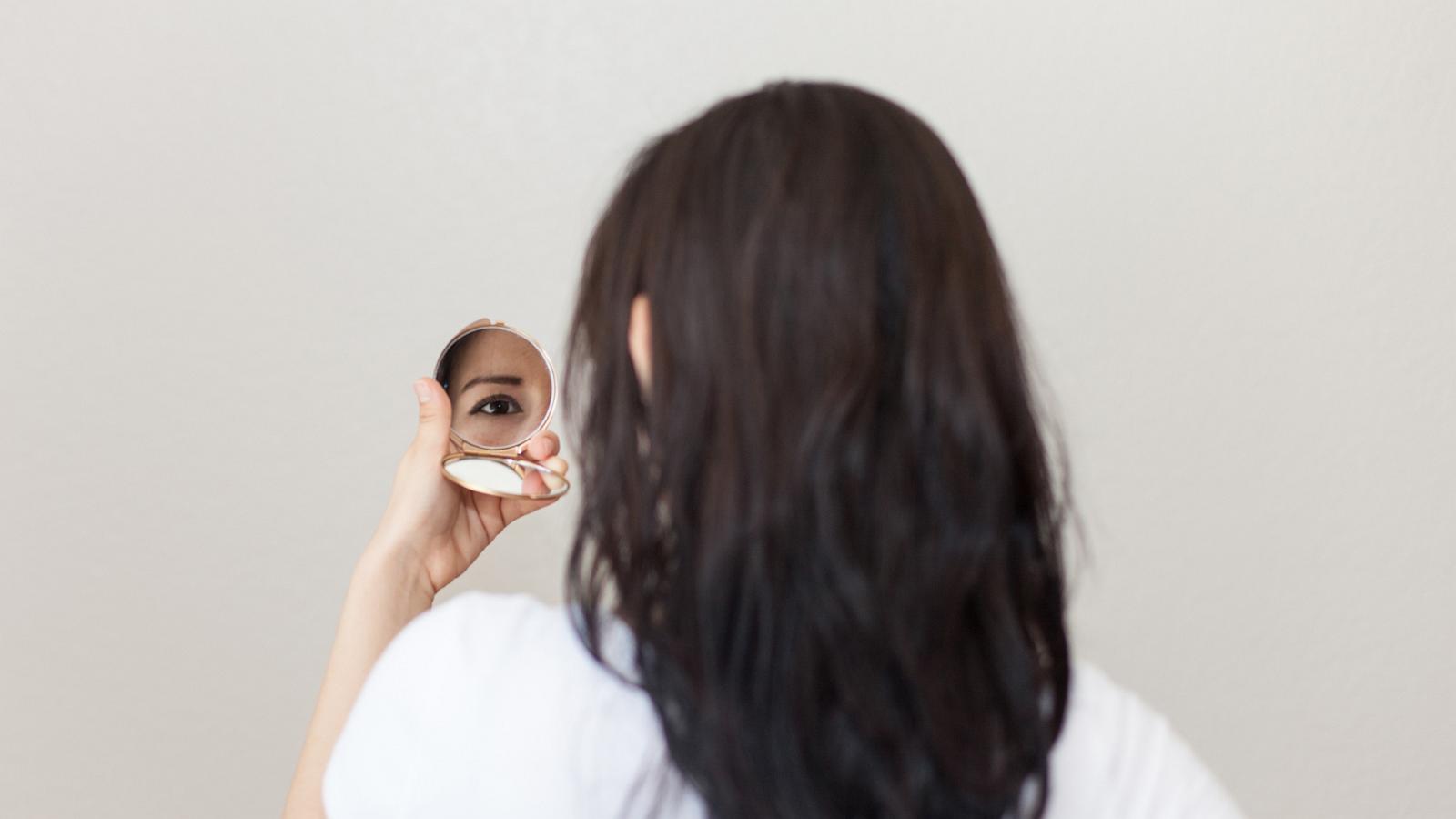 PHOTO: Woman looking at herself in small hand mirror