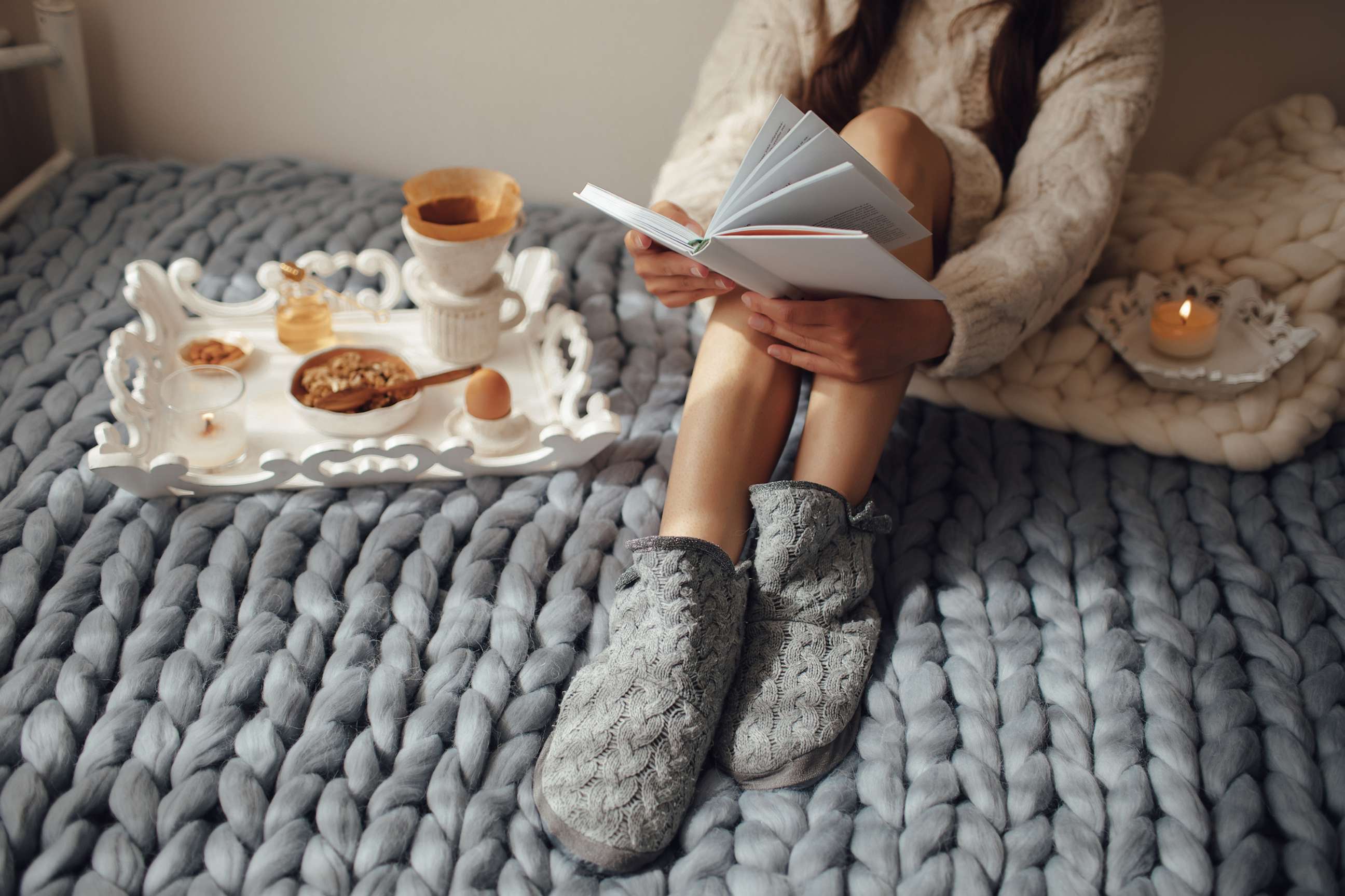 PHOTO: Woman with long hair drinking hot coffee and reading book in bed.