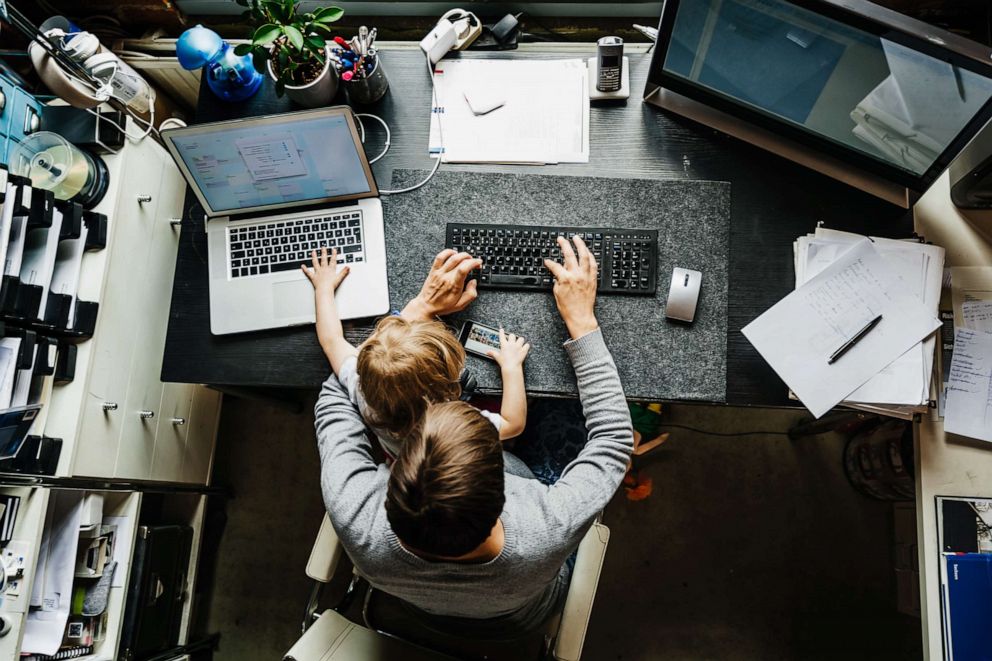 PHOTO: Stock photo of a mother working on a laptop in her office at home with her young daughter on her lap.