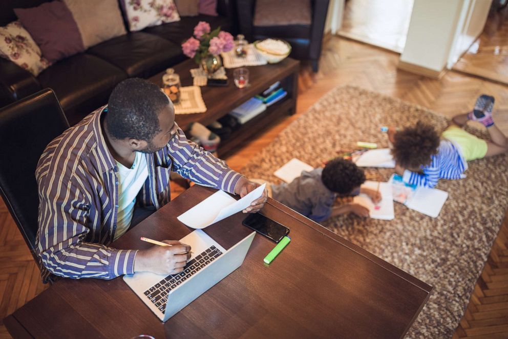 PHOTO: Stock photo of a father working from home with two children playing.