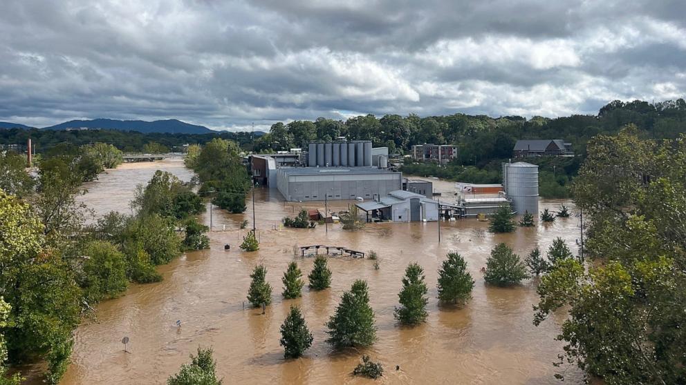 PHOTO: Bystanders watch the muddy waters of the French Broad River inundating the River Arts District in Asheville, NC, Sept. 28, 2024.