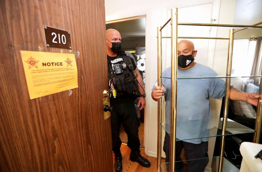 PHOTO: Milwaukee County Sheriff's Deputy Brian Green stands by as Rafael Hernandez, manager and truck driver with Eagle Movers and Storage Co., removes a shelf unit from an apartment during an eviction in Milwaukee, July 18, 2021.