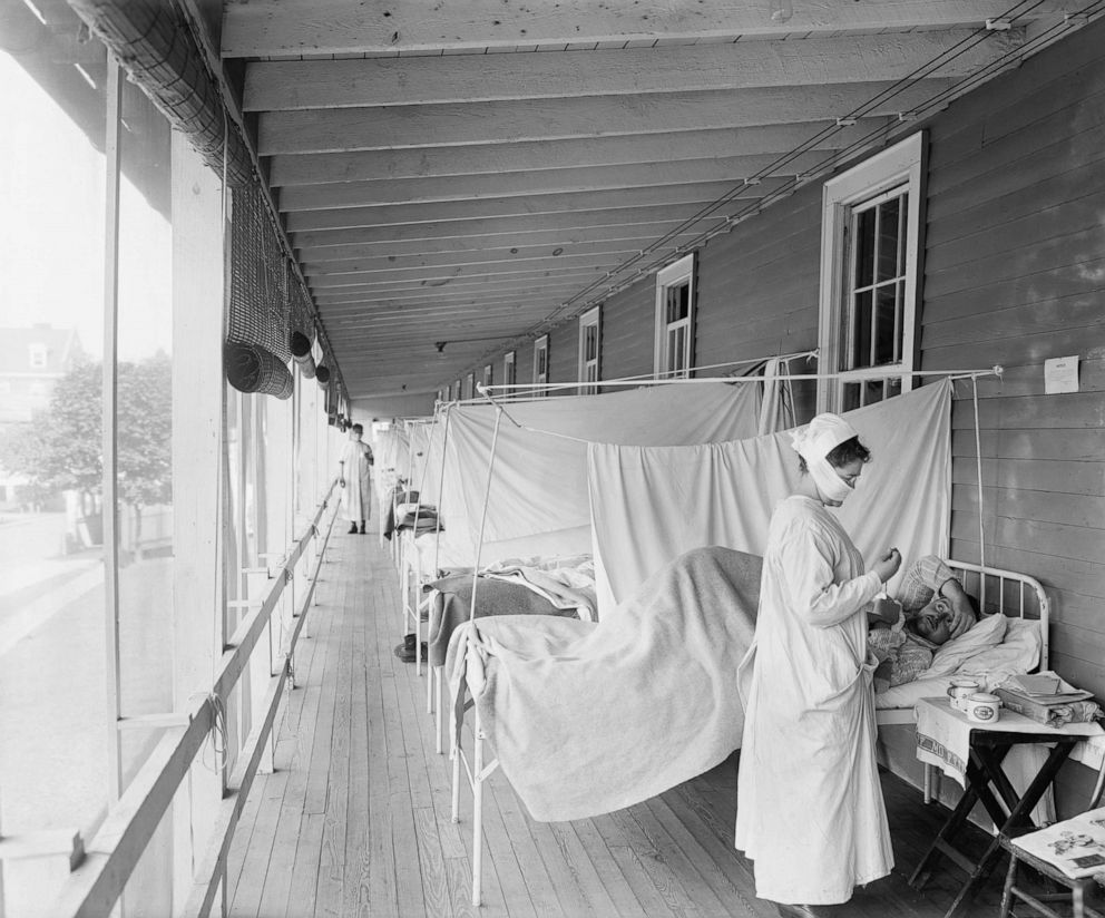 PHOTO: A masked nurse at the head of a row of beds treats patients during the influenza pandemic at Walter Reed Hospital, in Washington D.C., 1918.