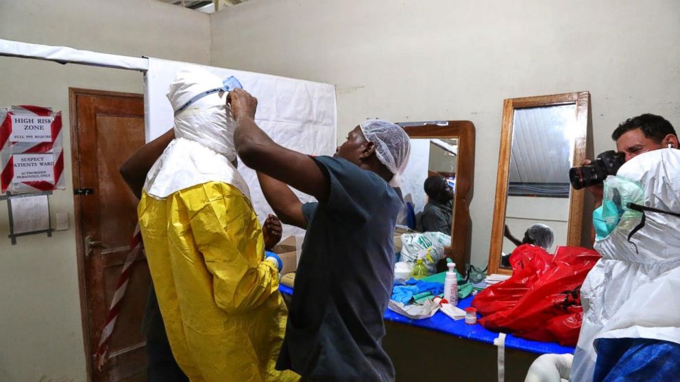 PHOTO: Three people help Dr. Besser put on protective gear outside the ELWA Ebola Isolation Unit in Monrovia, Liberia.