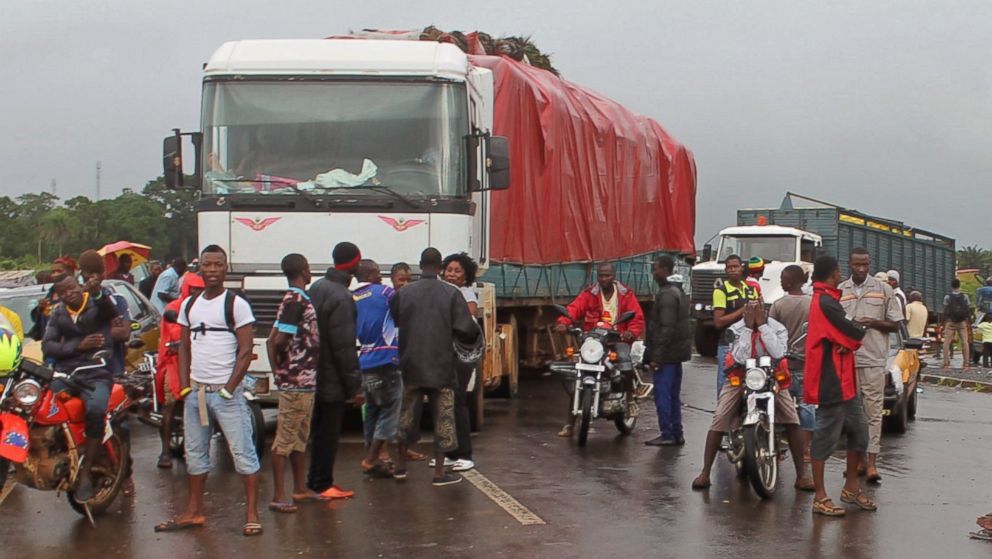 Stranded people stand behind a rope across the road that separates Guinea and Sierra Leone, and works as a makeshift border control checkpoint at Gbalamuya-Pamelap, Guinea, on Aug. 12,  2014. 