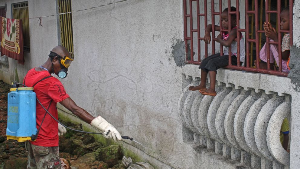 A man that was hired by the community sprays chemicals to try and prevent the spread of the Ebola virus, as local children look on, in Monrovia, Liberia, Aug. 29, 2014.  