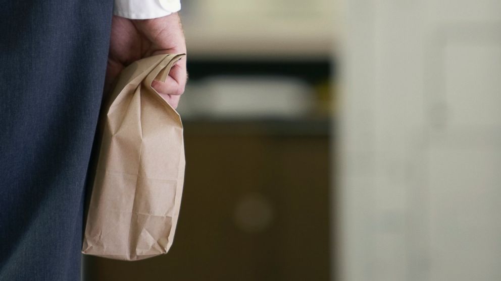 A businessman carries a paper lunch bag.