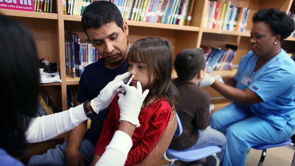 Jacquiline Lechuga ,5, sits on the lap of her father, Marko Lechuga as she receives an H1N1 nasal flu spray vaccine from nurse Shajaira Powell-Bailey at the Broadmoor Elementary school October 19, 2009 in Miami, Florida. 