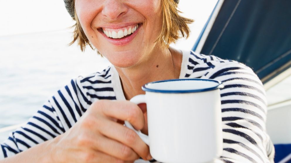 A woman is pictured smiling, while drinking coffee. 