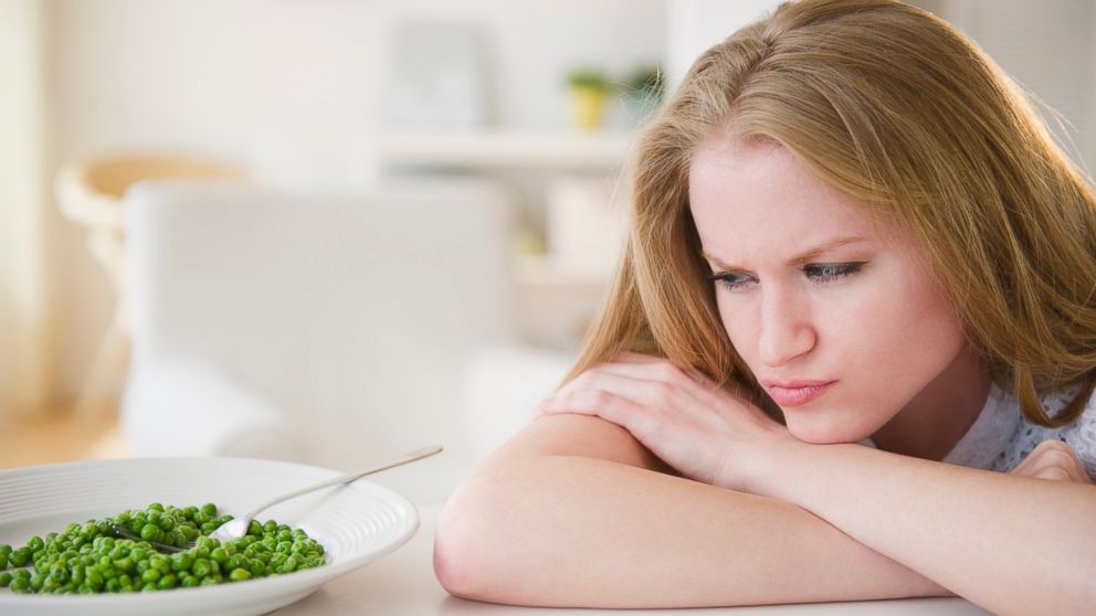 In this stock image, a woman angrily glares at a plate of green peas. 