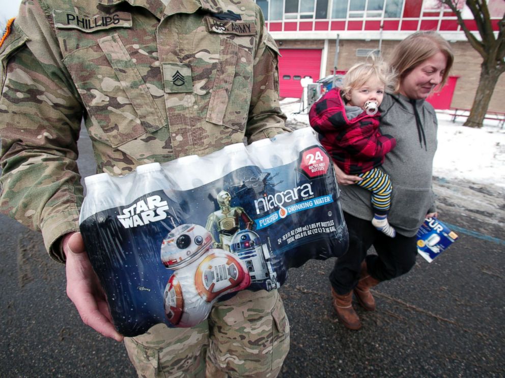 PHOTO: Michigan National Guard Staff Sergeant William Phillips of Birch Run, Michigan, helps Flint resident Amanda Roark and her son Dash take bottled water out to her vehicle after she received it at a Flint Fire Station Jan. 13, 2016 in Flint, Michigan.
