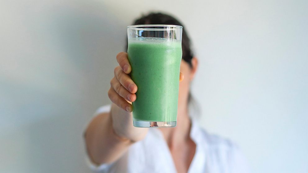 Woman holding up glass of fresh vegetable juice.