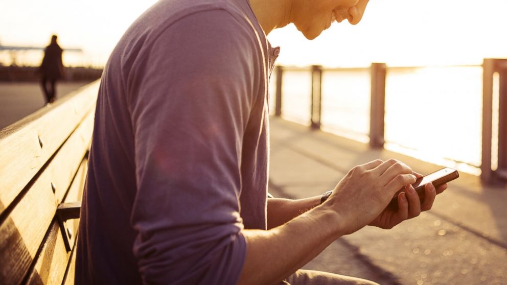 A young man using his smartphone in the par at sunset is seen. 