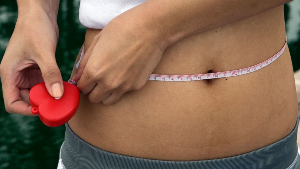 PHOTO: A woman measures her waistline using a tape measure.