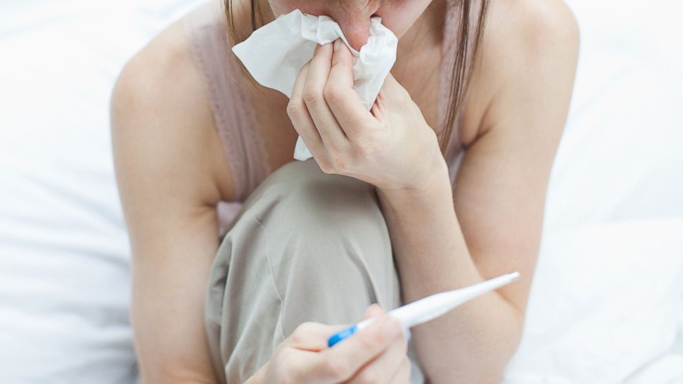 PHOTO: A sick woman takes her temperature with digital thermometer and blows nose in this stock photo.