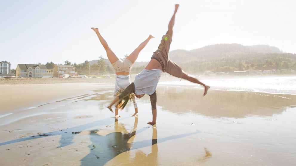 A stock image of a young couple doing cartwheels on beach. 
