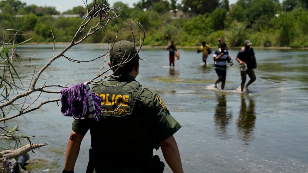 FILE - In this June 15, 2021, file photo, a Border Patrol agent watches as a group of migrants walk across the Rio Grande on their way to turning themselves in upon crossing the U.S.-Mexico border in Del Rio, Texas. A Justice Department attorney says
