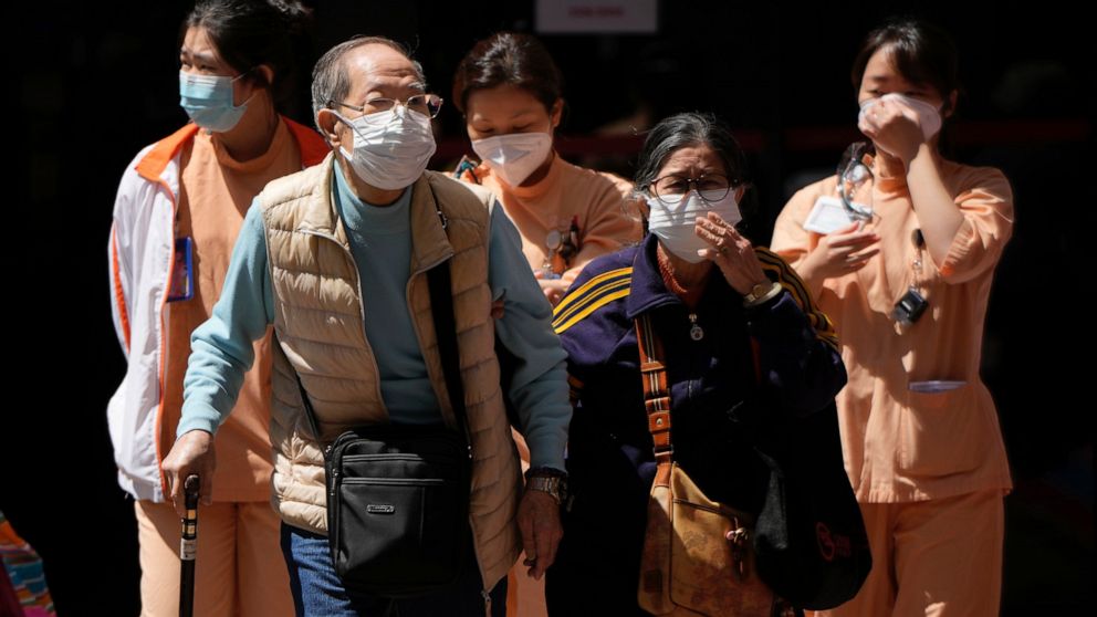 Elderly couple and medical staff walk out from the Queen Elizabeth Hospital in Hong Kong, Wednesday, March 9, 2022. Hong Kong leader Carrie Lam said Wednesday that there is "no specific time frame" for the testing exercise, as authorities focused the