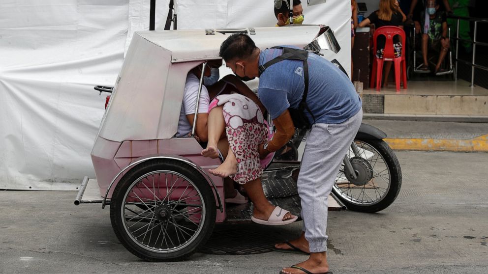 A man carries a sick woman from a pedicab as they bring her to the emergency area of the hospital that is crowded with suspected COVID-19 patients in Manila, Philippines on Monday, April 26, 2021. COVID-19 infections in the Philippines surged past 1 