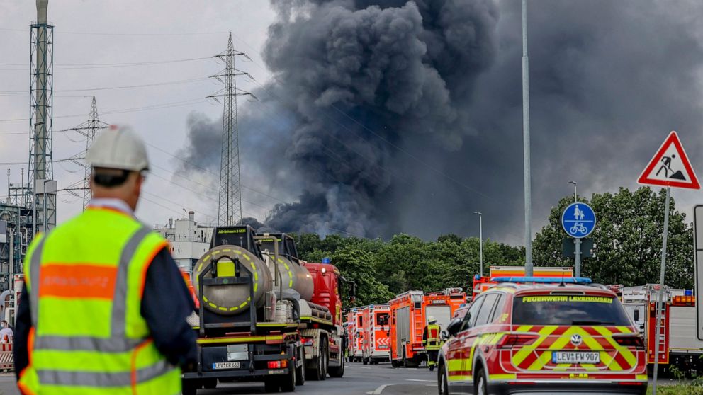 Emergency vehicles of the fire brigade, rescue services and police stand not far from an access road to the Chempark over which a dark cloud of smoke is rising in Leverkusen, Germany, Tuesday, July 27, 2021.. After an explosion, fire brigade, rescue 