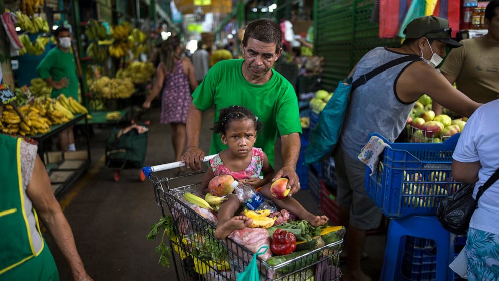 In this March 18, 2020 photo, Cesar Alegre, accompanied by his 4-year-old daughter Lia, places a damaged apple in his shopping cart filled with discarded produce given to him by vendors at a popular market in Lima, Peru. It is a task that was hard at