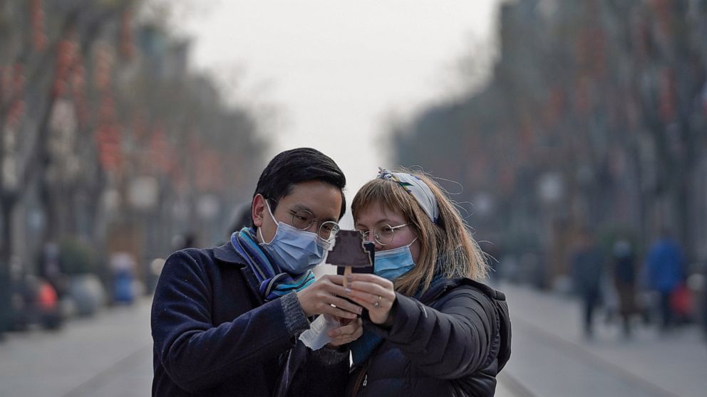 Visitors wearing face masks to help curb the spread of the coronavirus take a smartphone photo of an ice-cream with a shaped of Qianmen Gate which bought at Qianmen Street, a popular tourist spot in Beijing, Sunday, Jan. 31, 2021. A World Health Orga