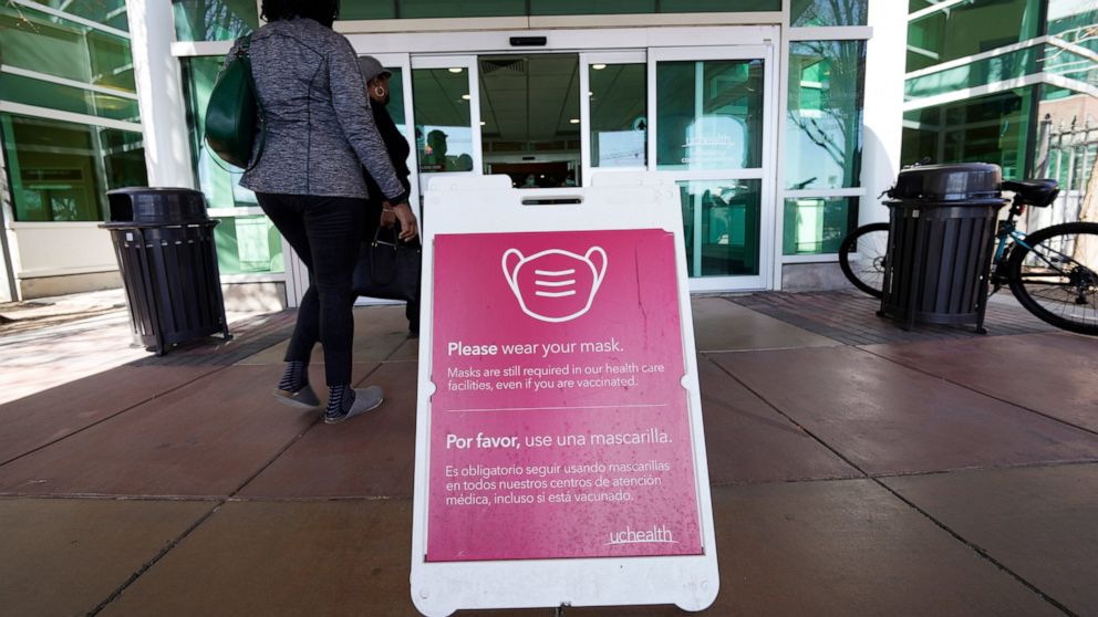 FILE - A sign advising visitors to don face coverings stands outside the main entrance to UCHealth University of Colorado hospital Friday, April 1, 2022, in Aurora, Colo. COVID cases are starting to rise again in the United States, with numbers up in