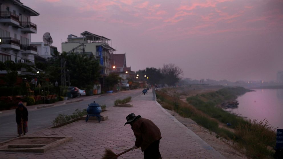 FILE - m municipal worker sweeps a pathway along the Mekong River Thursday, Dec. 12, 2013, in Vientiane, Laos. The landlocked Southeast Asian nation of Laos reopened to tourists and other visitors on Monday, more than two years after it imposed tight