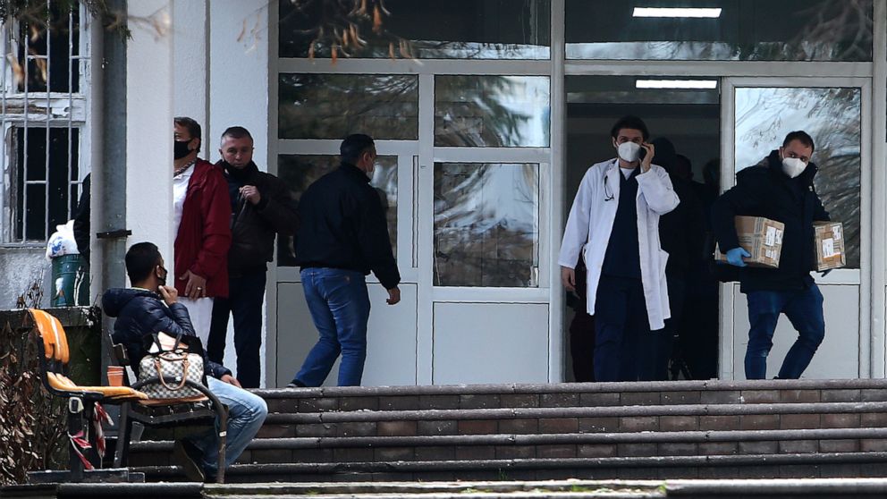 In this picture taken on Tuesday, Dec. 29, 2020, people and health workers are pictured in front of the entrance of the University Clinic complex in Skopje, North Macedonia. When thousands of people across the European Union simultaneously began roll