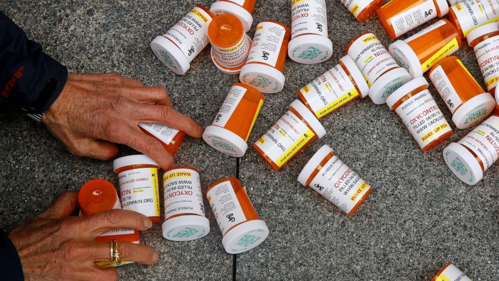 FILE - A protester gathers containers that look like OxyContin bottles at an anti-opioid demonstration in front of the U.S. Department of Health and Human Services headquarters in Washington on April 5, 2019. A California judge has ruled for top drug